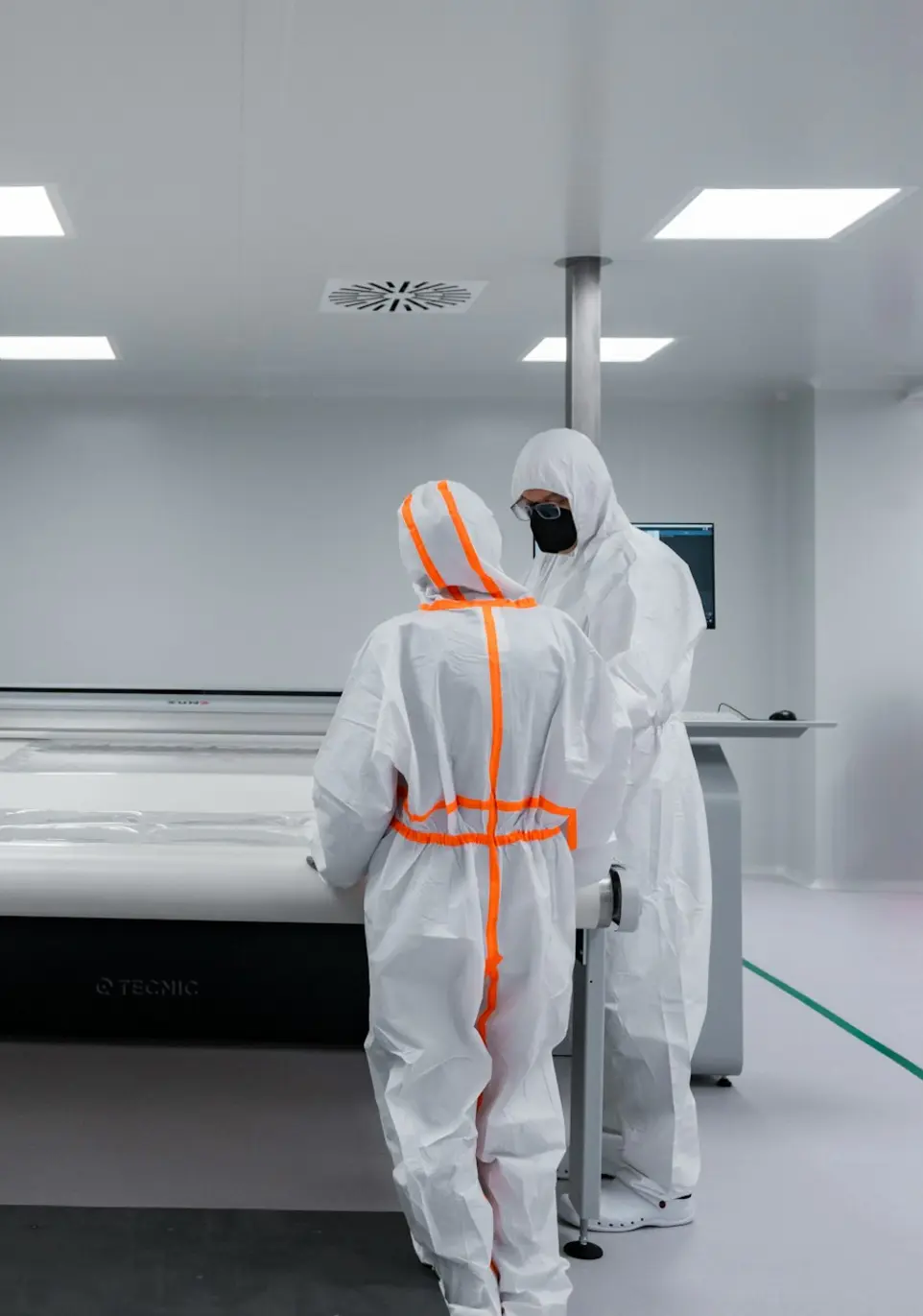 Workers in protective suits work in a cleanroom.